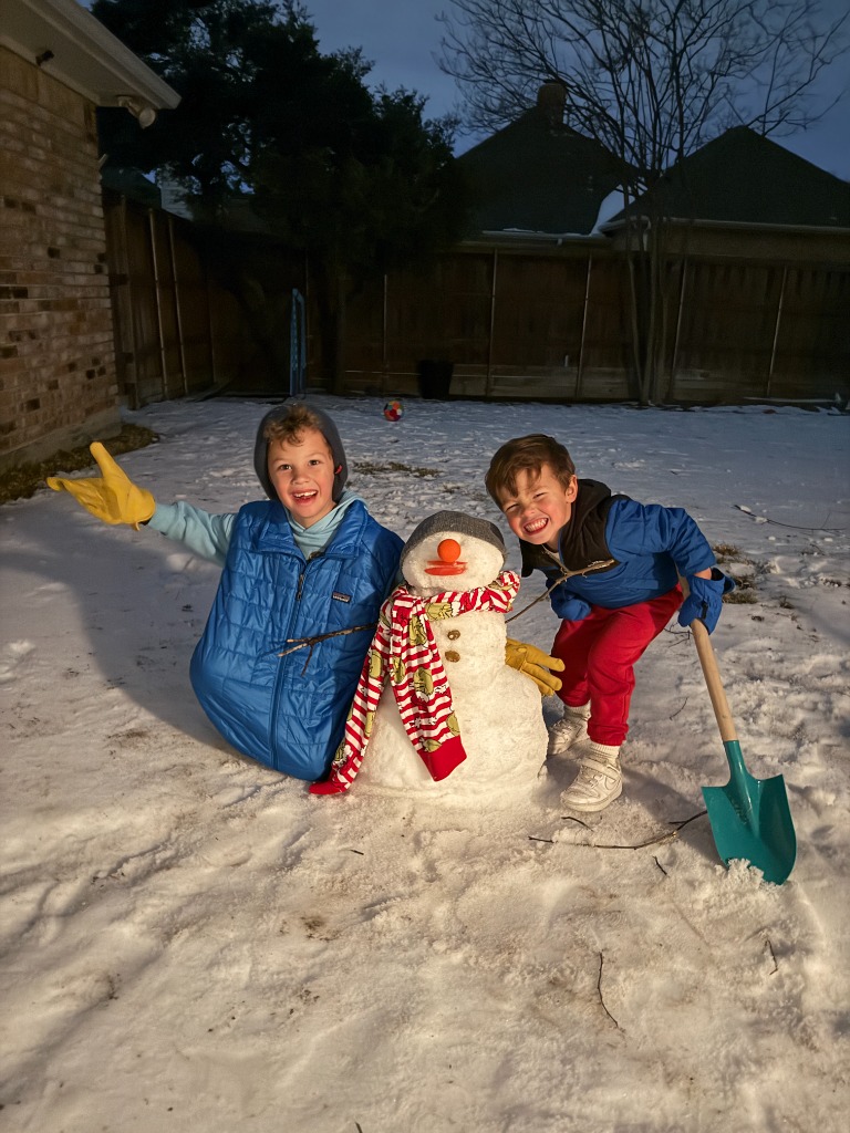 Two boys happily building a snowman in the backyard snow